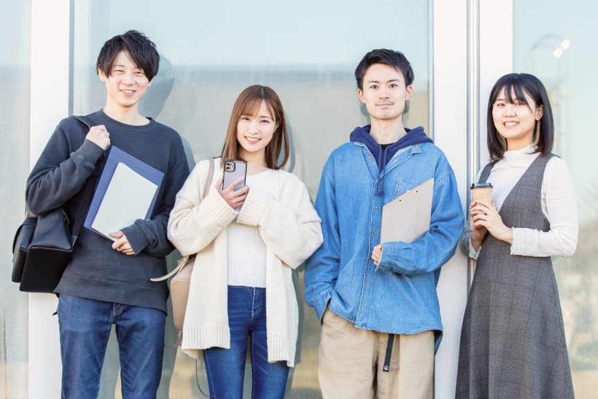 明るい笑顔の学生たちが校舎前で談笑している様子